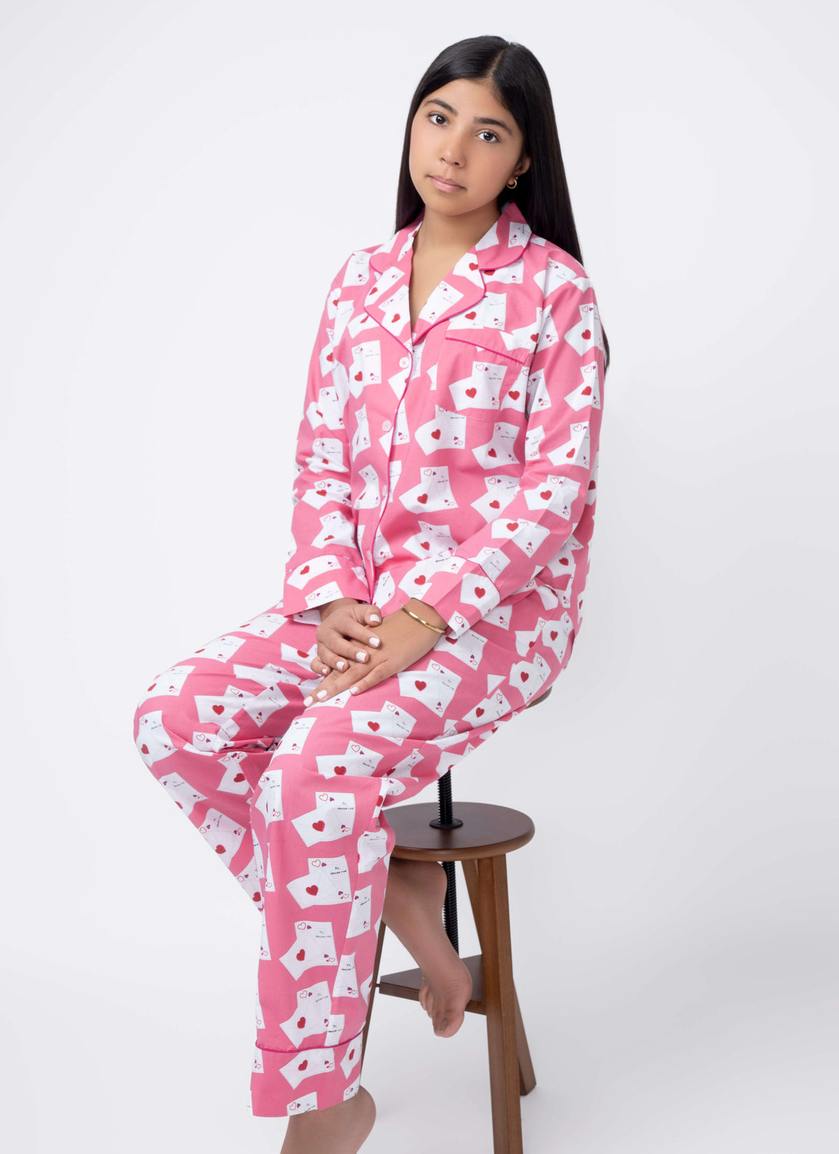 Woman wearing pink pajamas with white patterns sitting on a stool against a white background