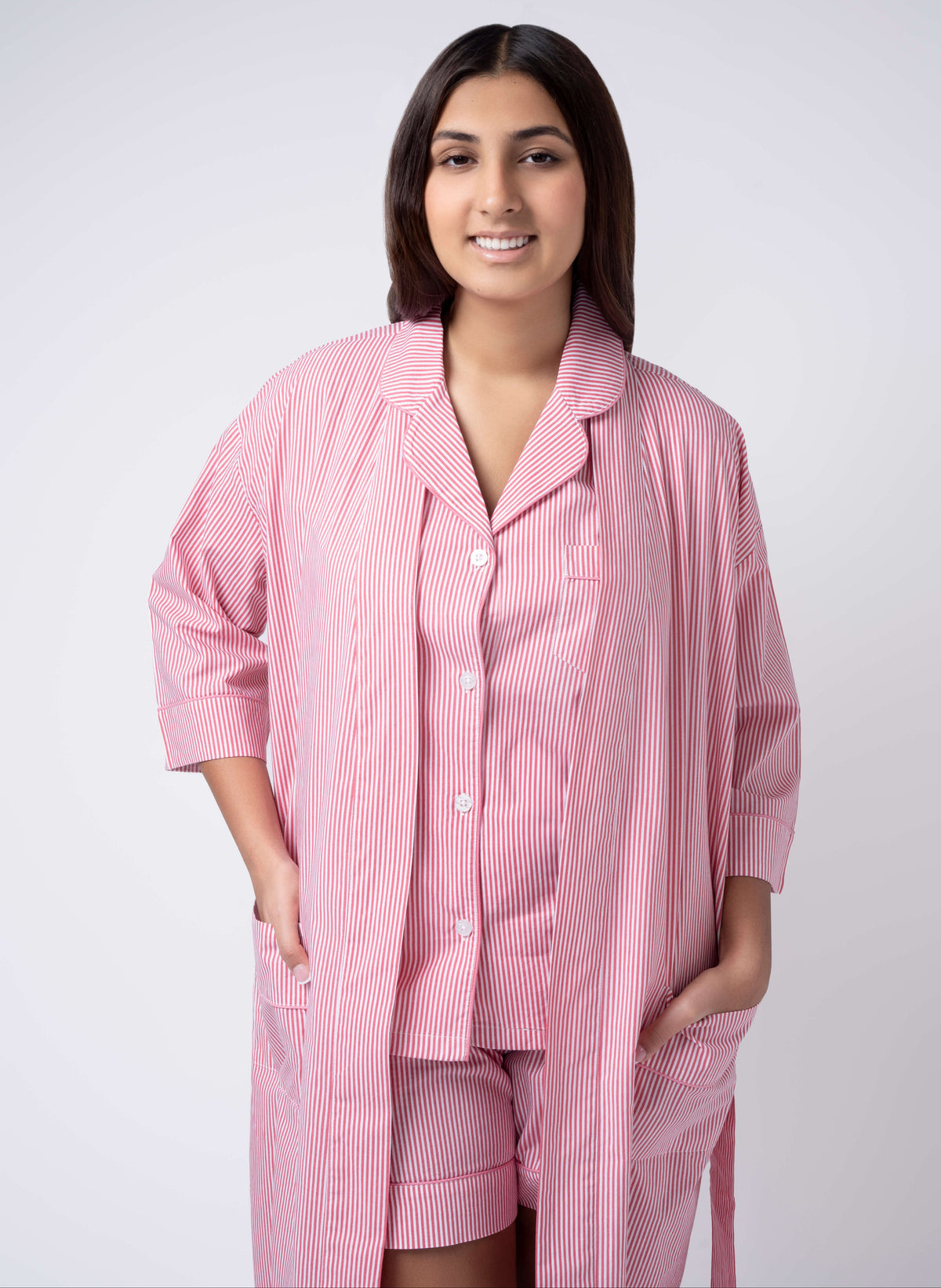 Woman wearing a pink checkered pajama set with a robe on a white background