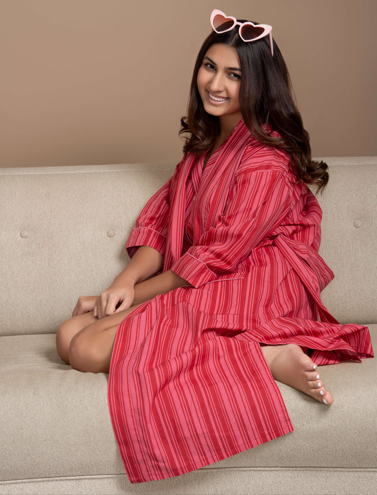 Woman wearing a red striped robe sitting on a beige couch with a neutral background
